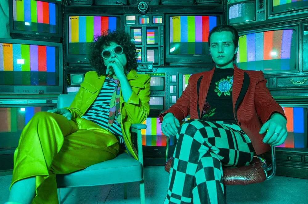 Artists in colourful outfits surrounded by vintage television screens